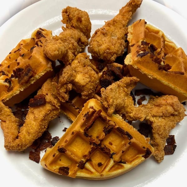 Crispy fried chicken pieces and waffles with bacon bits on a white plate at Sweet Berry Cafe.