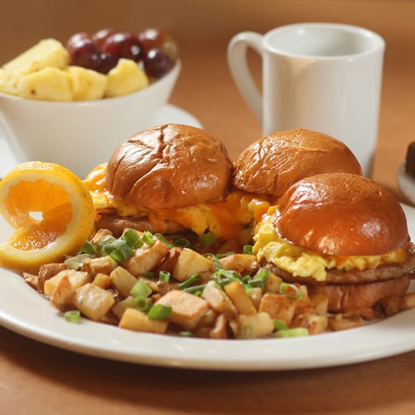 Three breakfast sliders with scrambled eggs, cheese, and sausage, served with home fries and fruit.