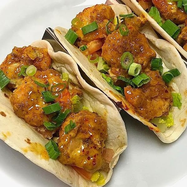 Three Sweet Berry Cafe tacos filled with crispy shrimp, lettuce, and green onions on a white plate.