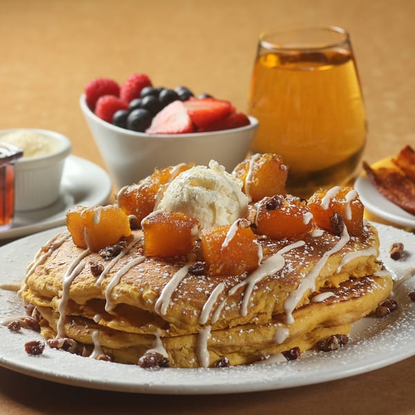 Sweet Berry Cafe's pumpkin pancakes with ice cream, fruit, and juice on a table.