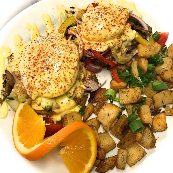 Sweet Berry Cafe's Eggs Benedict with home fries and an orange slice on a white plate.